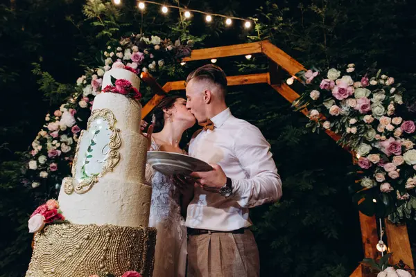 Gelin ve damat düğün töreninde düğün pastalarının yanında öpüşüyorlar.