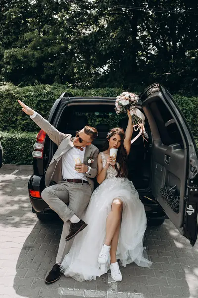 Güzel bir çift yeni evli arabada poz veriyor kola içiyor, gelin buketi kaldırıyor. 