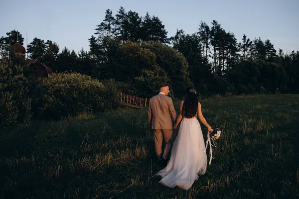 Düğün günü parkta yürüyen genç gelin ve damadın arka manzarası.   