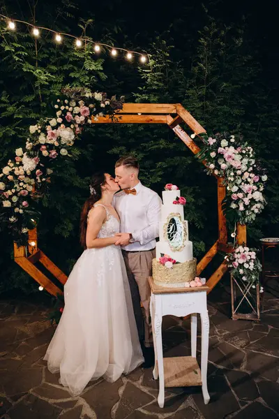 Gelin ve damat düğün töreninde düğün pastalarının yanında öpüşüyorlar.