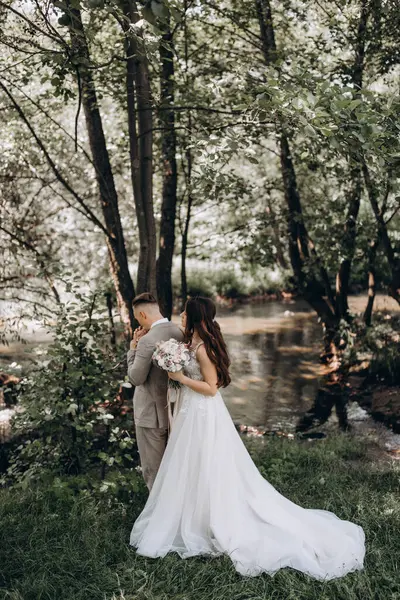 Güzel mutlu gelin ve damat gölün yakınındaki ormanda poz veriyor..          