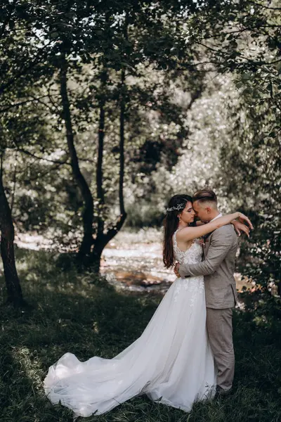 Güzel mutlu gelin ve damat gölün yakınındaki ormanda poz veriyor..          