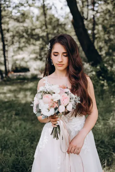 Yeşil parkta düğün buketi tutan güzel gelinin portresi.        