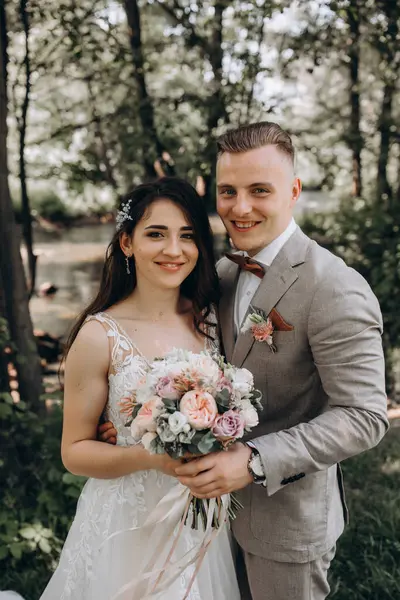 Güzel mutlu gelin ve damat gölün yakınındaki ormanda poz veriyor..          