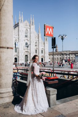 Şehir sokaklarında poz veren bir buket çiçekli mutlu gelin.  