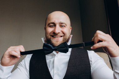 Genç damat takım elbise ve papyon giyip odada poz veriyor..