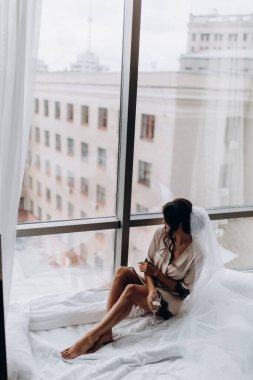 İpek bornoz ve peçeli güzel bir kadın şarap içiyor ve pencere eşiğinde dinleniyor.