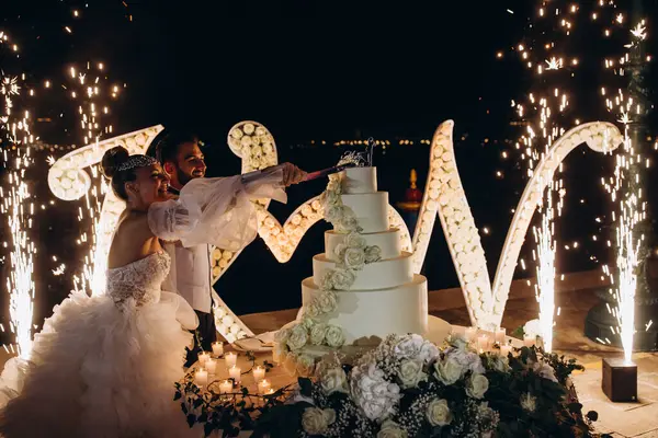 Mutlu genç gelin ve damat gece düğün pastası kesiyor.