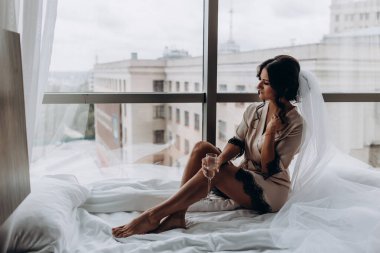 İpek bornoz ve peçeli güzel bir kadın şarap içiyor ve pencere eşiğinde dinleniyor.