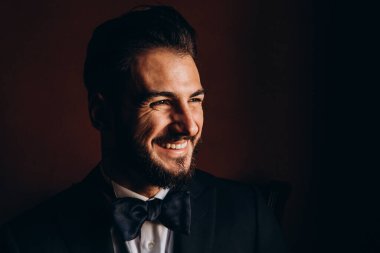 Şık takım elbiseli yakışıklı genç adam ve siyah duvar arkasında poz veren papyon.