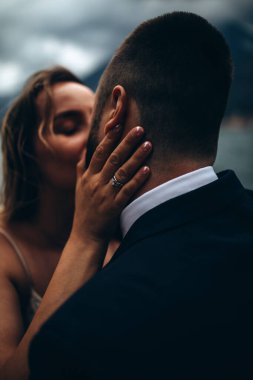 Genç gelin ve damat dağların ve gölün arka planında öpüşüyorlar.