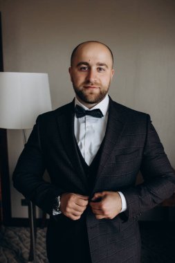 Genç damat takım elbise ve papyon giyip odada poz veriyor..