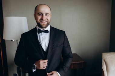 Genç damat takım elbise ve papyon giyip odada poz veriyor..