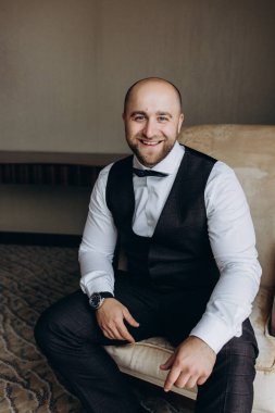 Genç damat takım elbise ve papyon giyip odada poz veriyor..