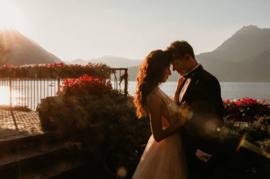 Gün batımında göl kenarında kucaklaşan genç gelin ve damat.       