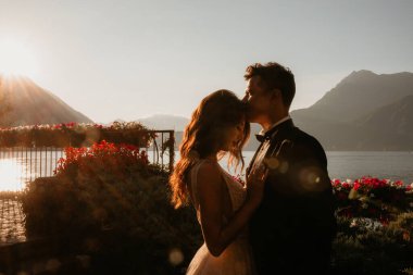 Gün batımında göl kenarında kucaklaşan genç gelin ve damat.       