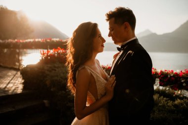 Gün batımında göl kenarında kucaklaşan genç gelin ve damat.       