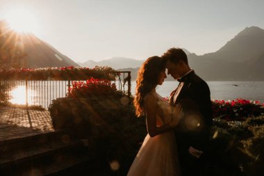 Gün batımında göl kenarında kucaklaşan genç gelin ve damat.       