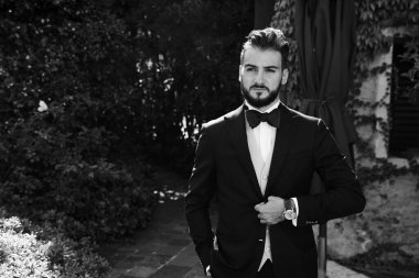 Şık damat sabahleyin siyah takım elbiseyle düğün için poz veriyor..