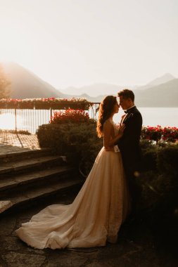 Gün batımında göl kenarında kucaklaşan genç gelin ve damat.       