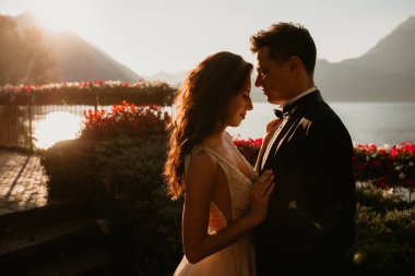 Gün batımında göl kenarında kucaklaşan genç gelin ve damat.       