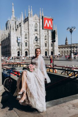 Şehir sokaklarında poz veren bir buket çiçekli mutlu gelin.  