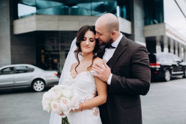 Mutlu yeni evliler şehrin arka planında sarılıyorlar.