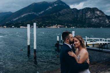 Birbirine aşık genç bir çift dağların ve gölün arka planında sarılıyor.