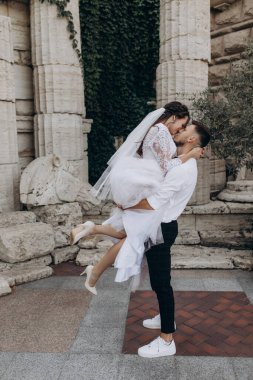 Mutlu düğün çifti eski sütunların yanında sarılıp öpüşüyor.