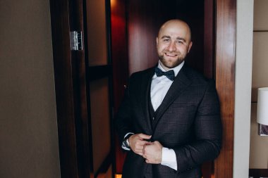 Takım elbiseli genç adam odada poz veriyor.