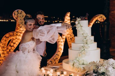 Mutlu gelin ve damat düğün pastasını çiçeklerle kesiyor.        