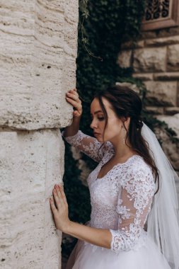 Beyaz gelinlikli genç güzel kız eski sütunun yanında poz veriyor.