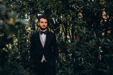 Siyah takım elbiseli yakışıklı damat ve papyon ormanın arka planında duruyor. 