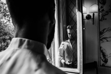 Adam aynanın önünde siyah beyaz poz veriyor.  