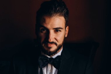 Zarif siyah takım elbiseli yakışıklı genç adam kameraya poz veriyor.