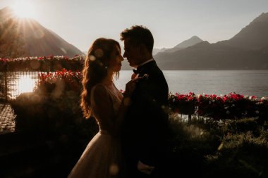 Gün batımında göl kenarında kucaklaşan genç gelin ve damat.       