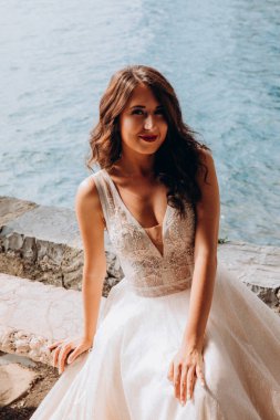 Güzel gelin düğün günü gölün kenarında oturuyor ve kameraya gülümsüyor.