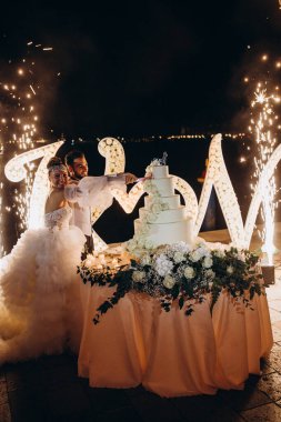 Mutlu gelin ve damat düğün pastasını çiçeklerle kesiyor.        