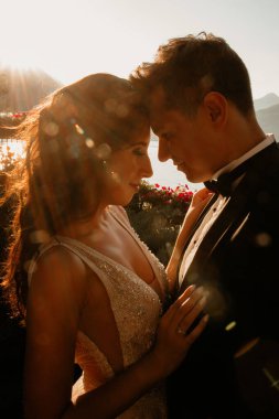 Gün batımında göl kenarında kucaklaşan genç gelin ve damat.       