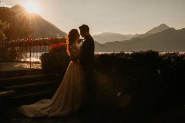 Gün batımında göl kenarında kucaklaşan genç gelin ve damat.       