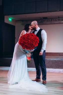 Öpüşen bir çift, elinde kırmızı gül çiçekleri tutan bir gelin.