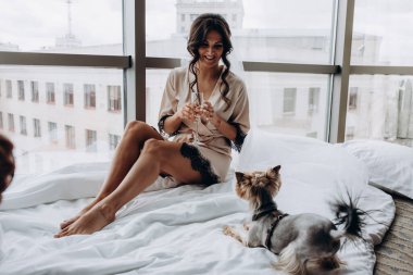 İpek bornoz ve peçeli güzel bir kadın şarap içiyor ve evde şirin küçük bir köpekle oynuyor.               