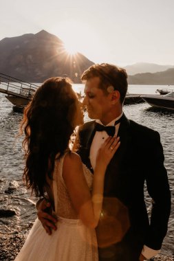 Mutlu genç gelin ve damat gün batımında sahilde öpüşüyor.