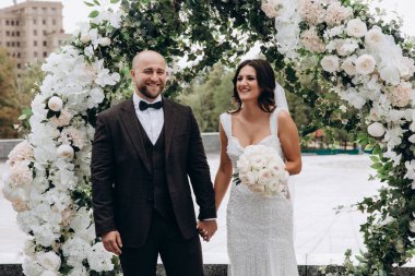 Mutlu gelin ve damat düğün gününde el ele tutuşup gülümsüyor.