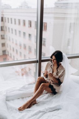 İpek bornoz ve peçeli güzel bir kadın şarap içiyor ve pencere eşiğinde dinleniyor.