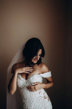 Duvak takmış, gülümseyen ve içeride poz veren gelinlik içinde güzel bir gelin.