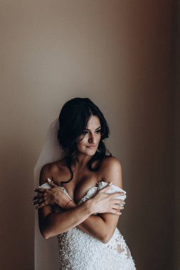 Gelinlik ve duvak giymiş, odada poz veren genç bir kadının portresi. 