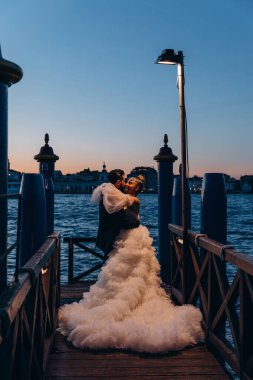 Venedik şehrinin güzel günbatımı manzarası ve kumsalda kucaklaşan düğün çifti.       