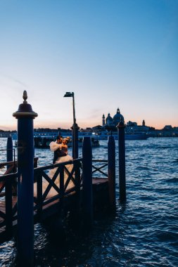 Venedik şehrinin güzel günbatımı manzarası ve kumsalda kucaklaşan düğün çifti.       