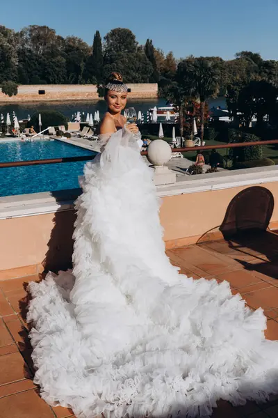 Gelinlikli güzel gelin güneşli bir günde havuz kenarında şarap içiyor.    